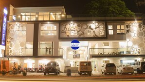 A modern hotel with a prominent 'ONE AVENUE' sign, a 'HOTEL' sign, and a '1A EXPRESS HOTEL' logo. There are multiple vehicles parked in front, including cars and a van. - 1A Express Hotel (Cagayan de Oro)