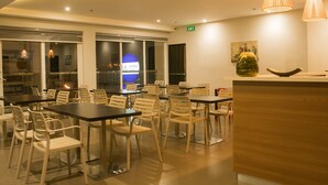 A modern hotel lobby with glass doors, a reception desk, and several tables and chairs. - 1A Express Hotel (Cagayan de Oro)