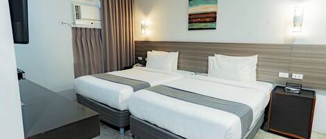 A hotel room with two beds, a desk, a nightstand, and a painting on the wall.