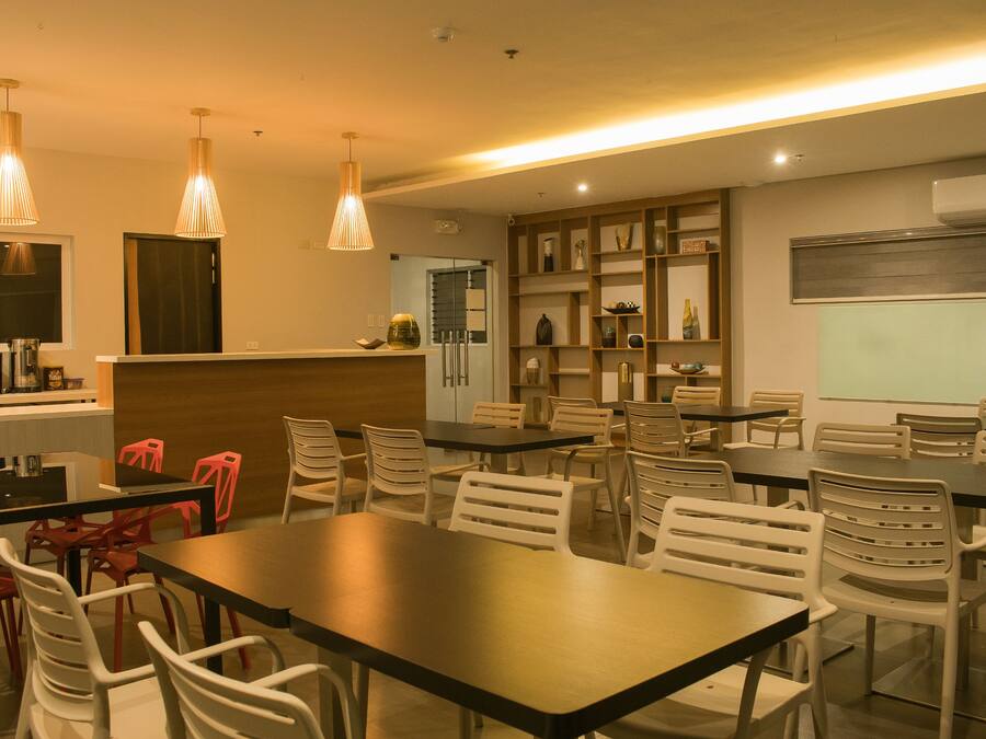 A modern dining area with multiple tables and chairs, pendant lighting, and a kitchen area in the background.