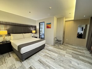 Quarto de hotel moderno com uma cama grande, mesa de cabeceira com abajur, espelho, cadeira e guarda-roupa.