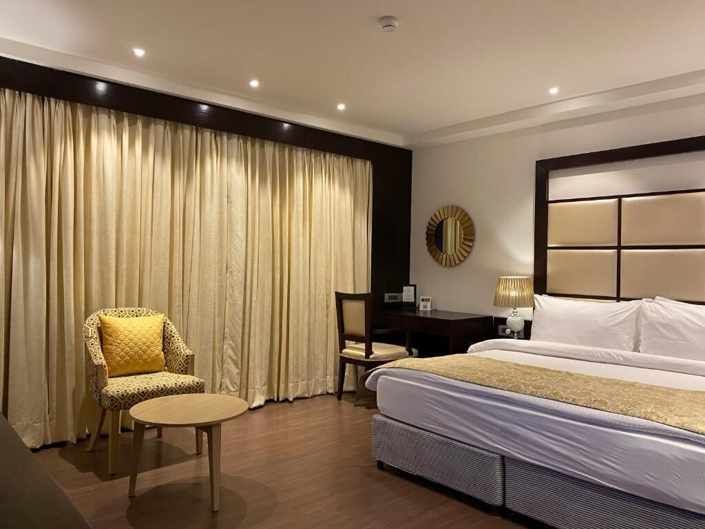 Une chambre d’hôtel avec un lit, une chaise, un bureau et une grande fenêtre avec des rideaux.