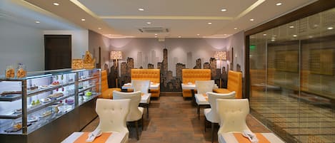 A restaurant with a cityscape wall mural, multiple seating options, and a dessert display.