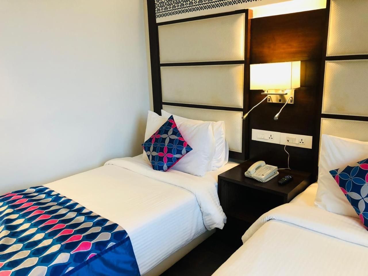 Habitación de hotel con dos camas, una mesita de noche con teléfono y una lámpara de pared.