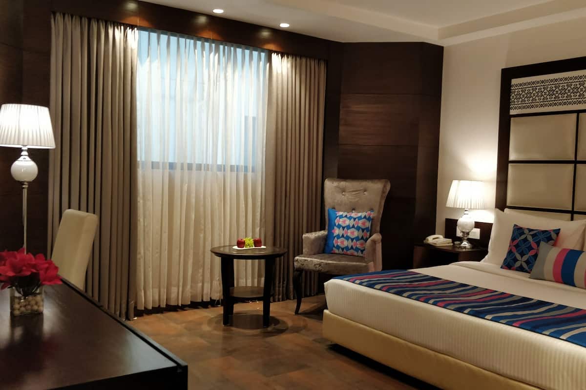 A hotel room with a large bed, a chair, a small table, and a desk with a lamp.