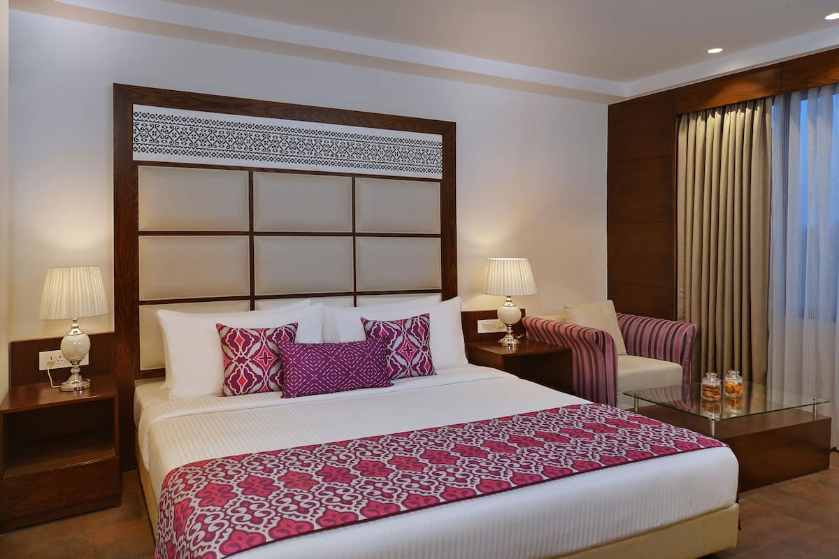 A hotel room with a large bed, two bedside tables, a chair, a glass coffee table, and a window with curtains.