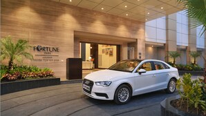 Ein weißer Audi parkt vor einem Gebäude, an dem Schilder mit den Aufschriften "Fortune Park" und "Haridwar Mitglied der ITC Hotel Gruppe" angebracht sind.