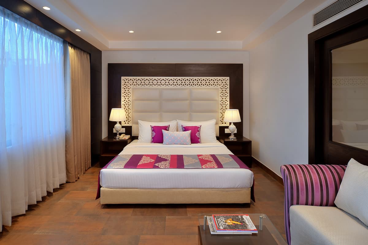 A hotel room with a large bed, two bedside tables with lamps, a sofa, and a coffee table.