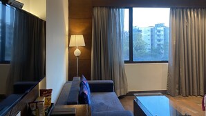 Ein modernes Hotelzimmer mit großem Flachbildfernseher, einer Couch, einem Glastisch und einer Lampe.