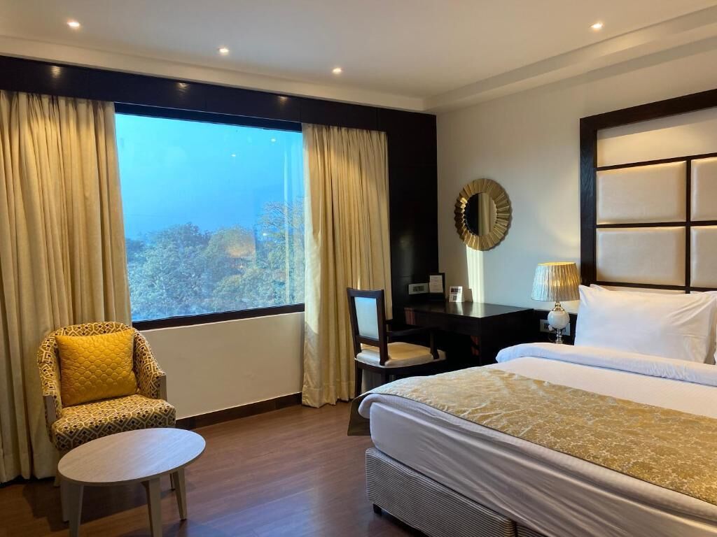 Ein Hotelzimmer mit einem großen Bett, einem Schreibtisch, einem Sessel, einem kleinen Tisch und Blick ins Freie.