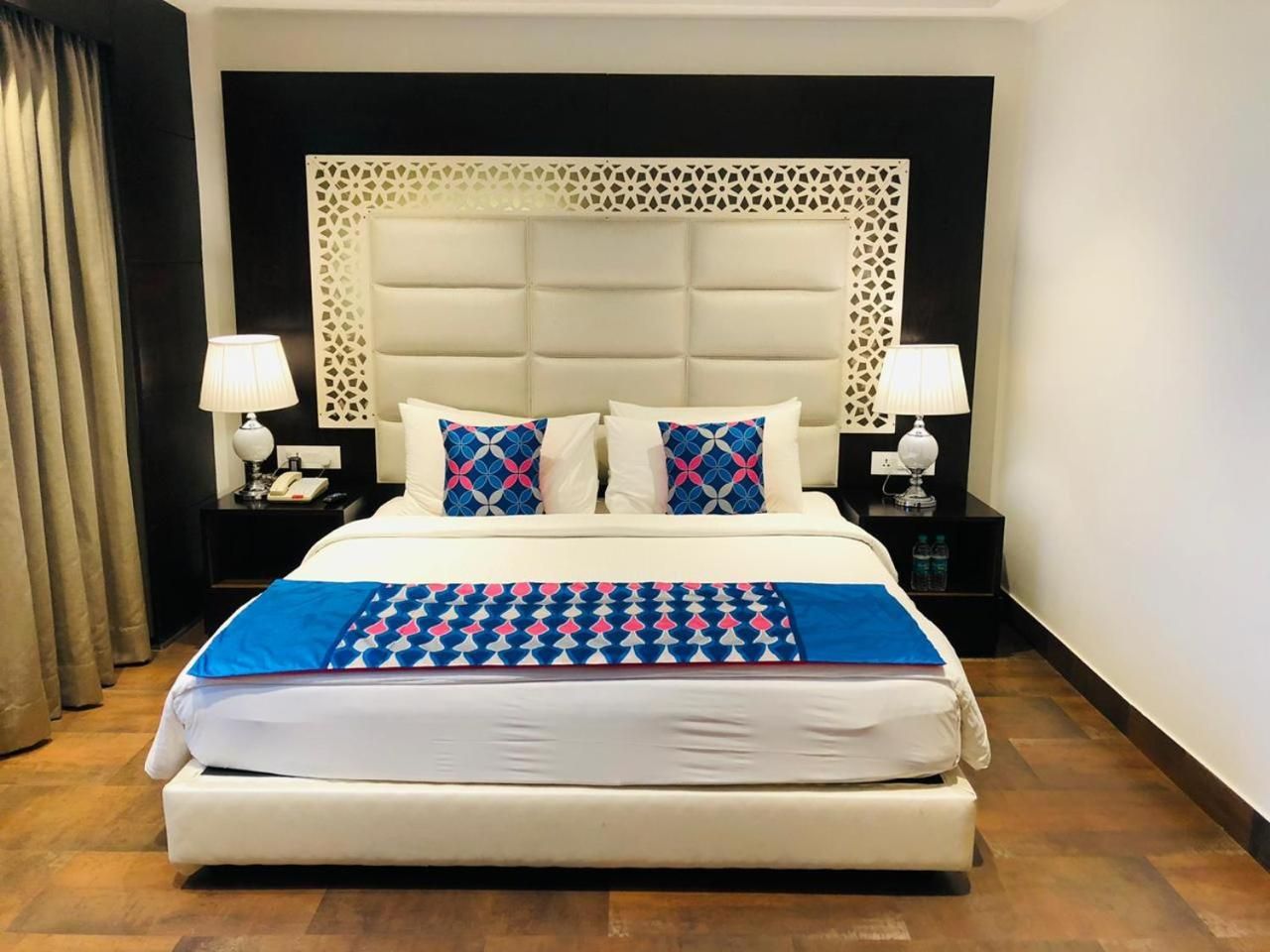 A hotel room with a large bed, two bedside tables with lamps, a decorative headboard, and a patterned throw blanket.
