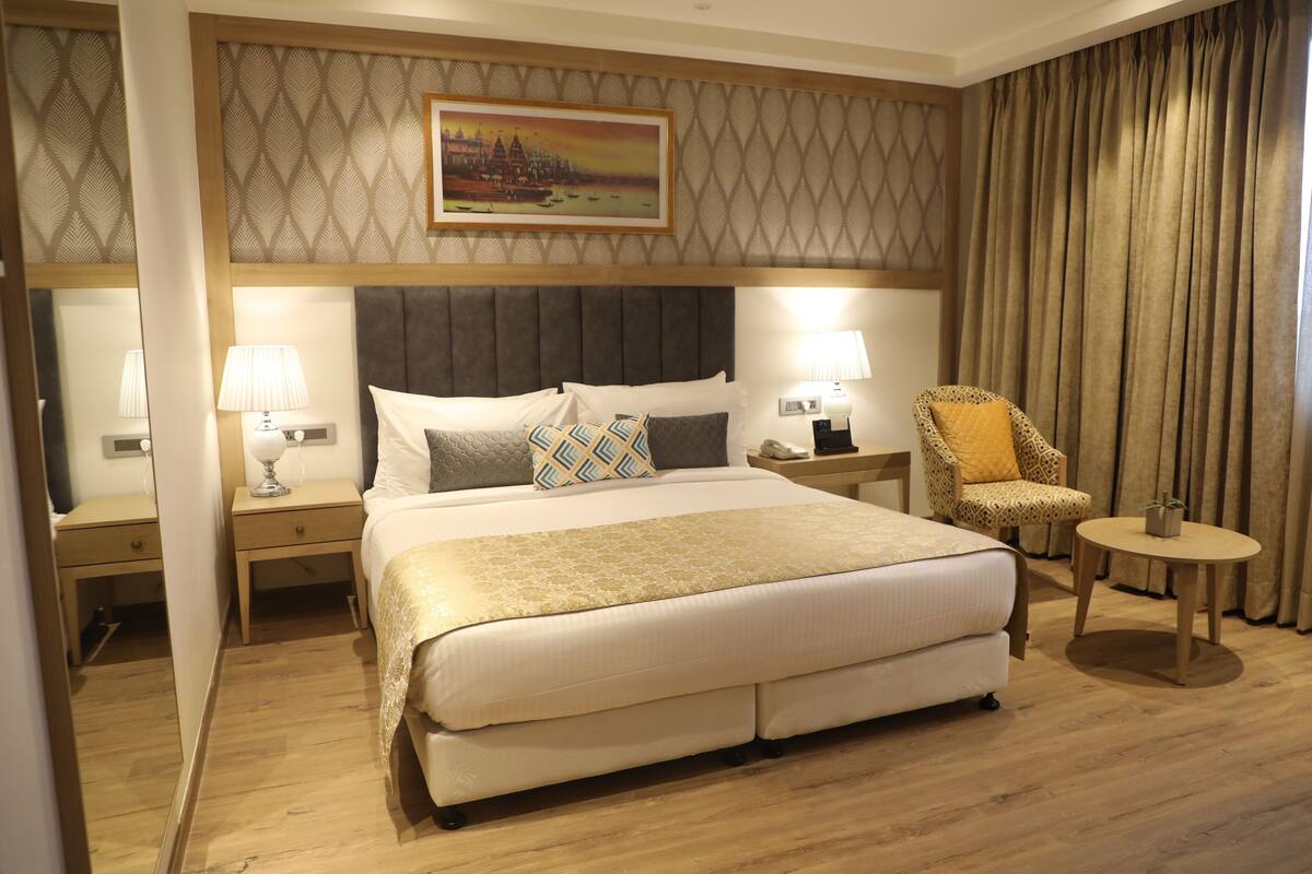 A hotel room with a large bed, two bedside tables with lamps, a chair, and a painting on the wall.