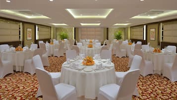 A banquet hall with round tables, white chairs, and floral centerpieces.