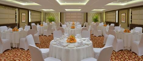 A banquet hall with round tables, white chairs, and floral centerpieces.