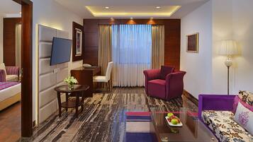 A hotel room with a bed, a desk with a chair, a sofa, a TV, and a lamp.