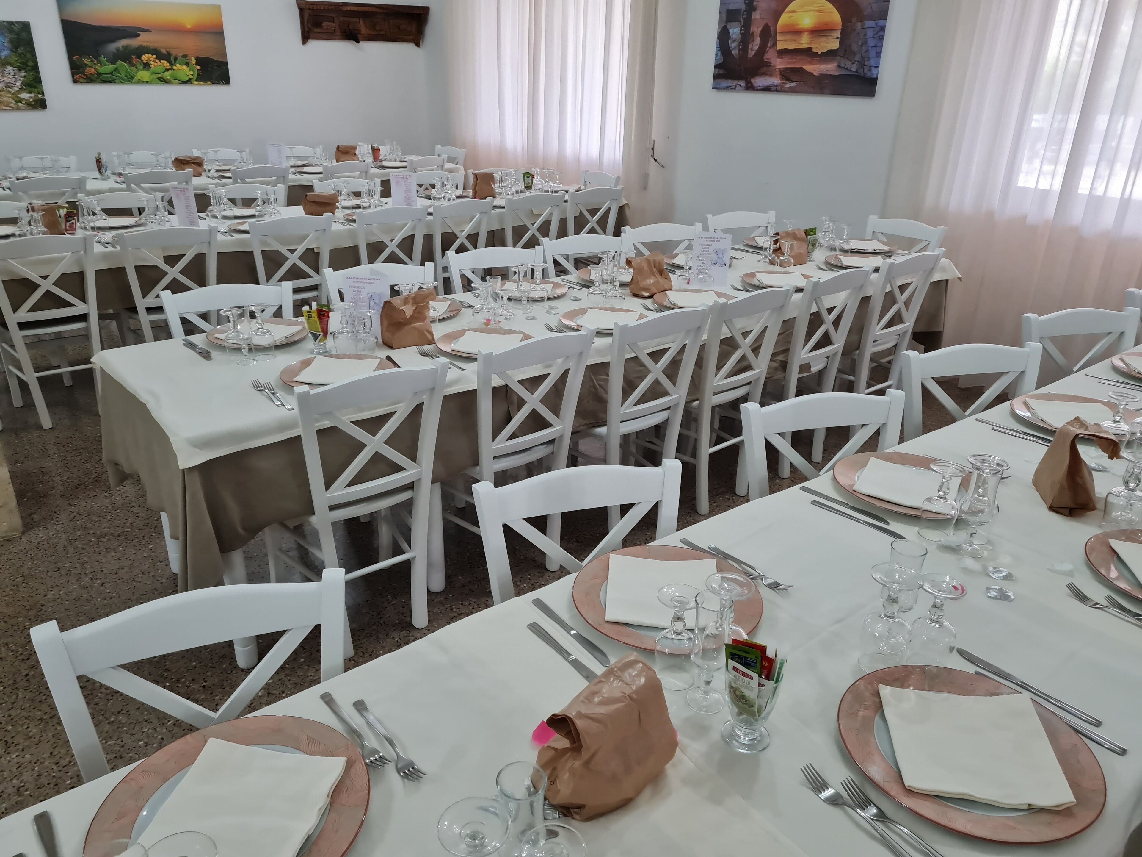 A dining area with multiple tables set for a meal, white chairs, and various dining utensils.