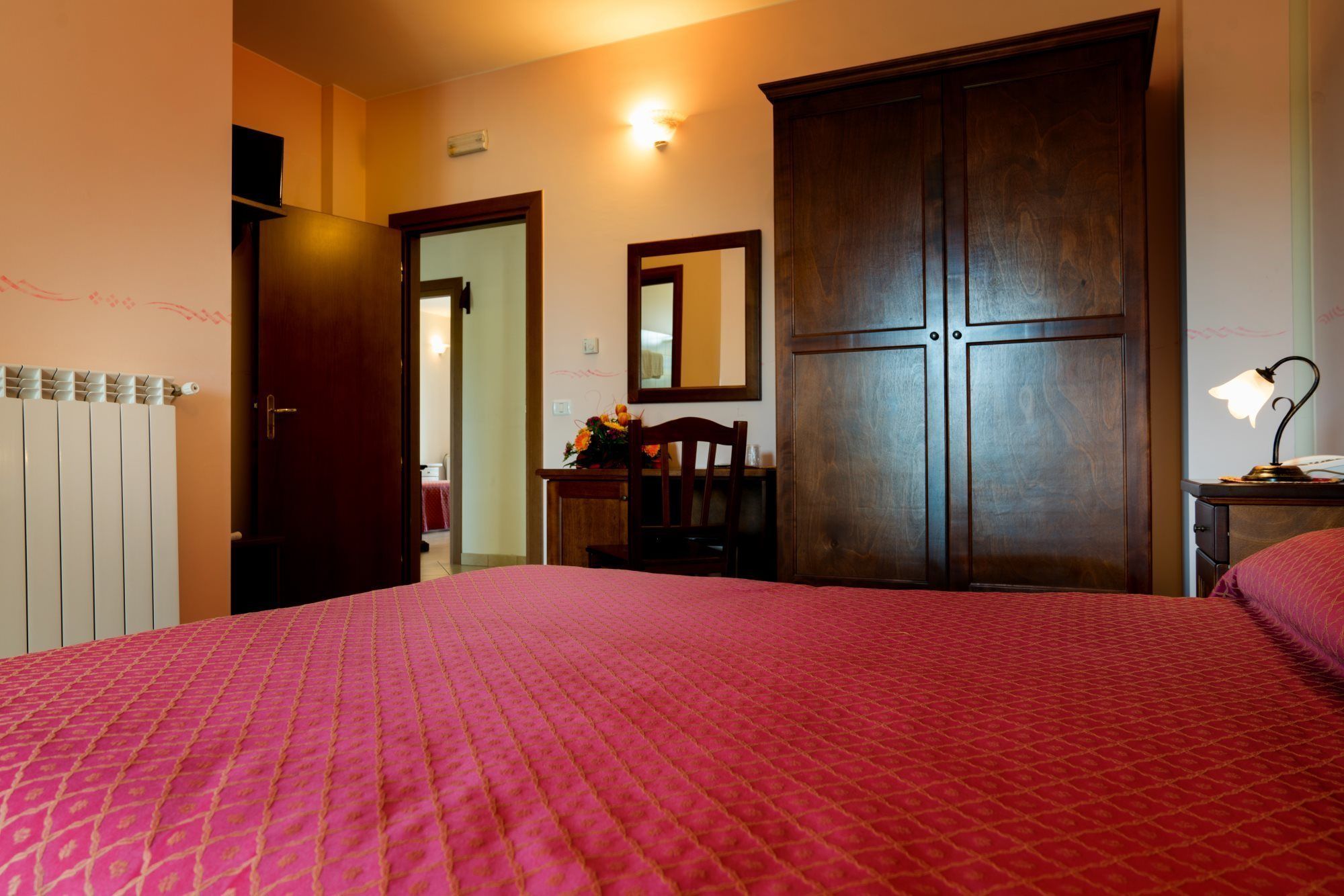 Ein Schlafzimmer mit einem großen Bett, einem Holzschrank, einem Schreibtisch mit Stuhl, einem Spiegel und einem Heizkörper.