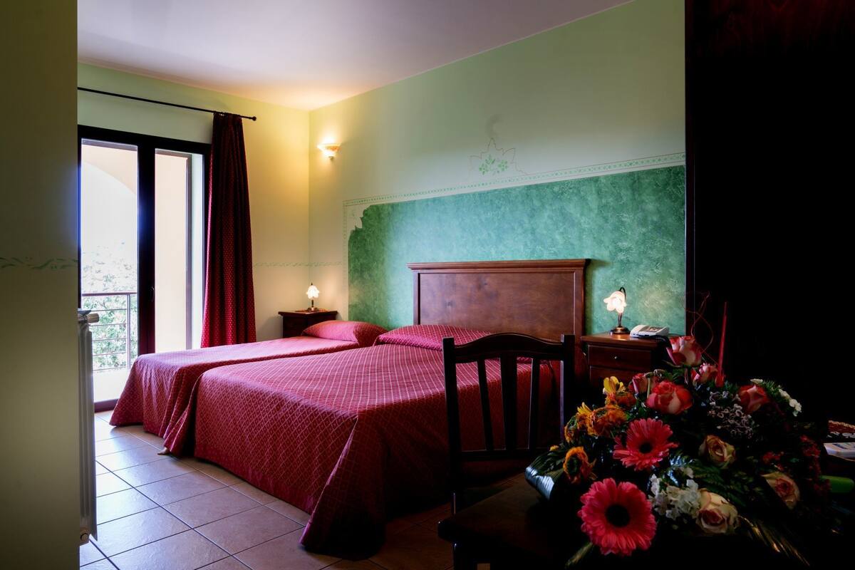 Un dormitorio con dos camas, una mesita de noche, un aparador, una lámpara y un arreglo floral.