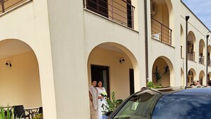 A black car parked in front of a building with arched balconies and outdoor seating. - Hotel Salento (Specchia)