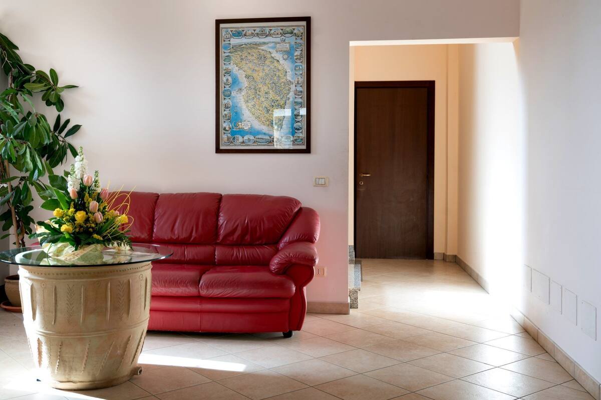 Una sala de estar con un sofá rojo, una planta grande en maceta y un mapa enmarcado en la pared.