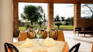 A covered outdoor dining area with tables set for two, featuring yellow tablecloths and black chairs. - Hotel Salento (Specchia)