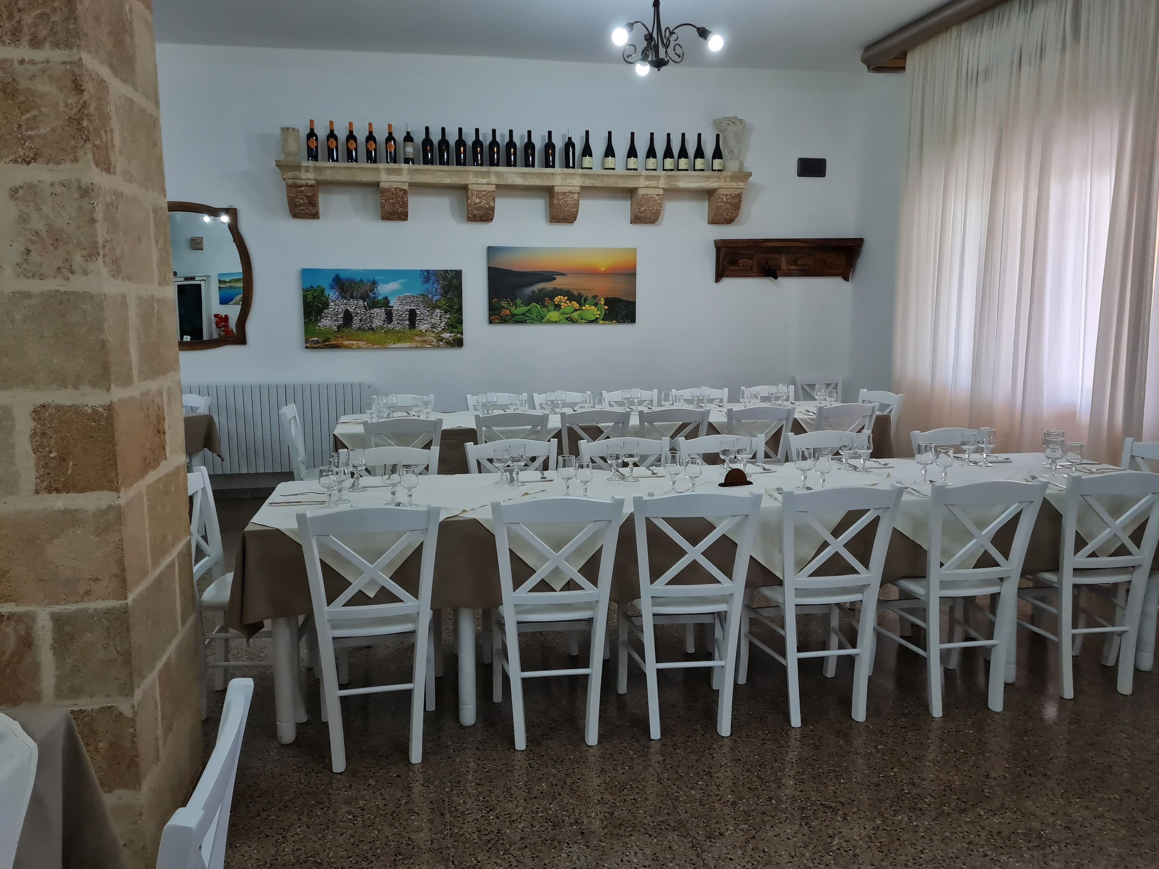 Ein Essbereich mit weißen Tischen und Stühlen, einem Weinregal mit Flaschen und zwei Bildern an der Wand.