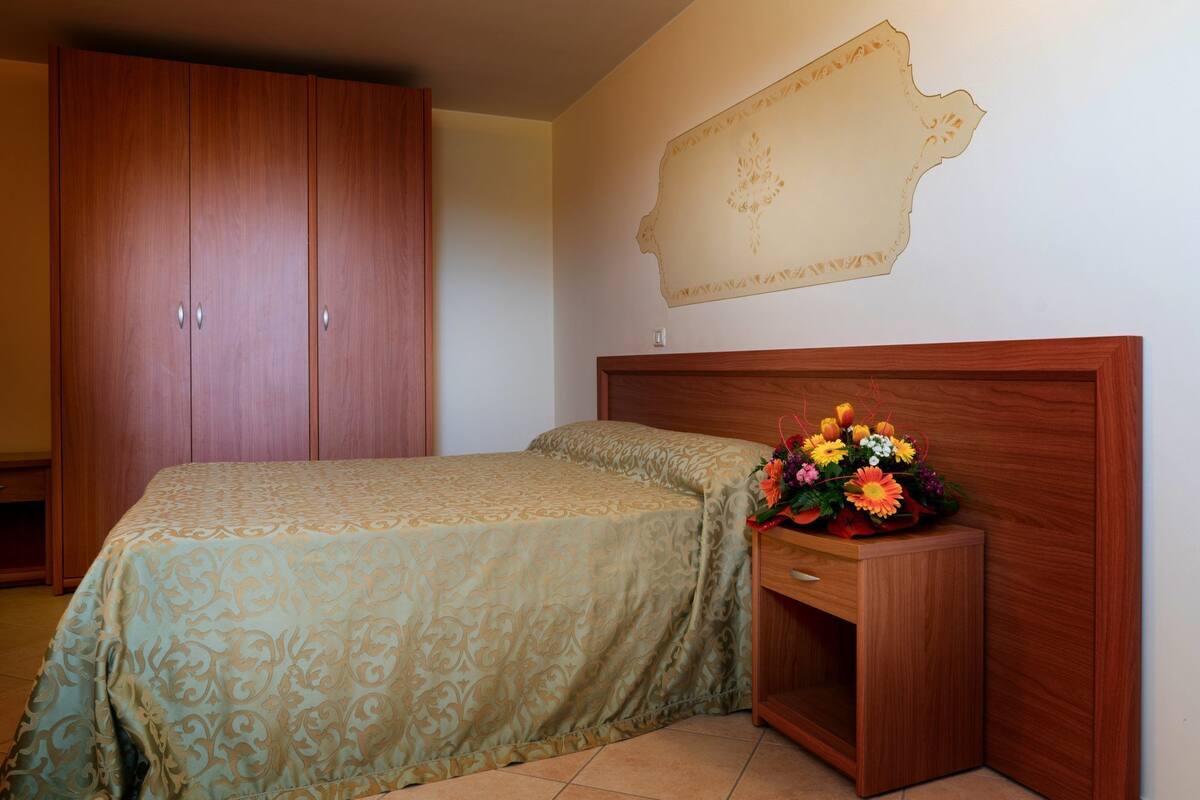 Un dormitorio con una cama, un armario de madera, una mesita de noche con un jarrón de flores y un mapa en la pared.