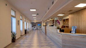 Un hall de hotel con mostrador de recepción, zona de descanso y pantalla de televisión.