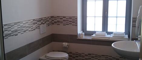 A bathroom with a toilet, bidet, and sink. There is a window with blinds and a towel rack.