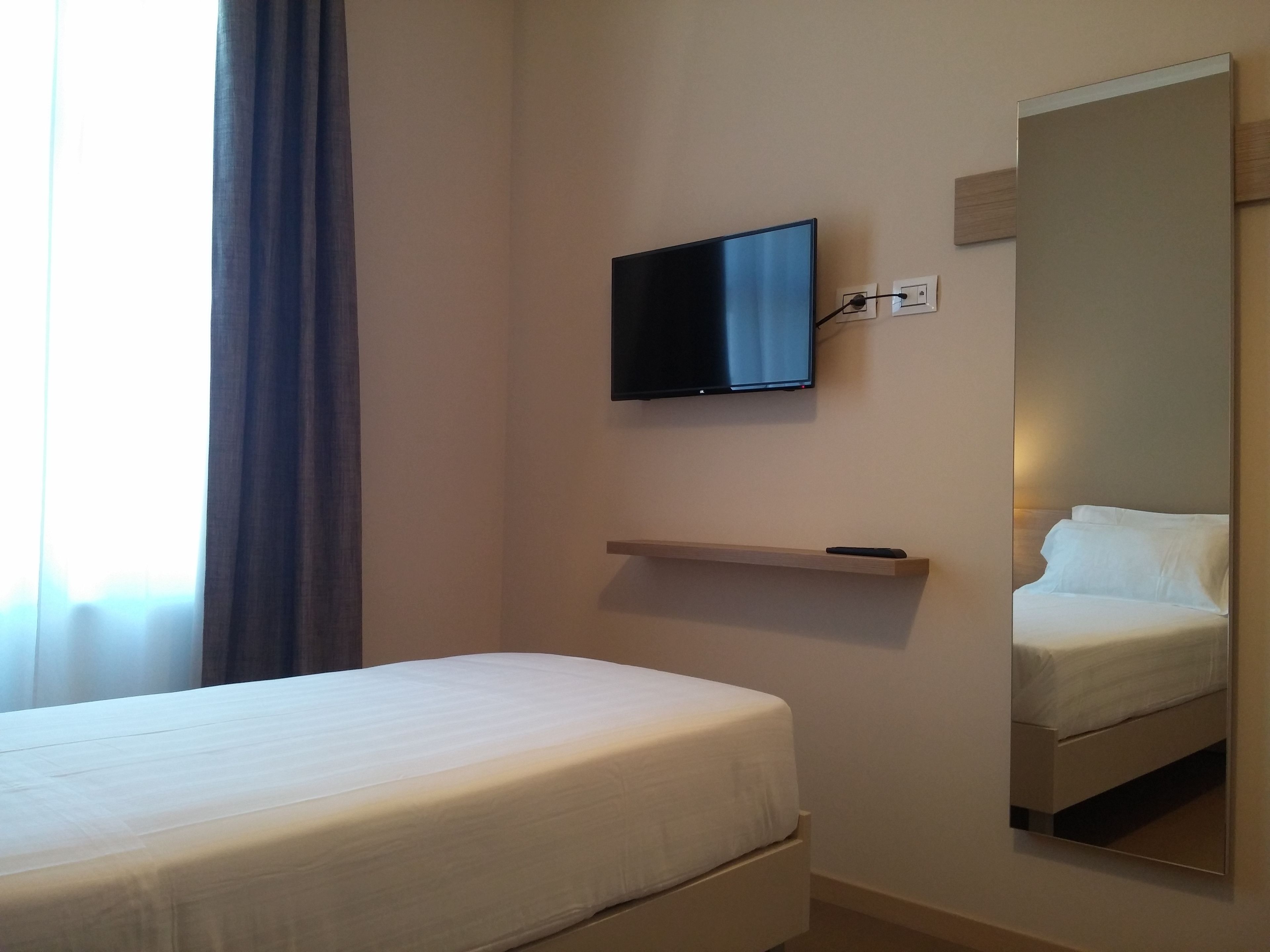 Quarto de hotel com cama, televisão na parede e um espelho grande.