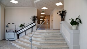 Una escalera moderna y luminosa con barandilla, plantas en macetas y un carrito de equipaje en un espacio interior.