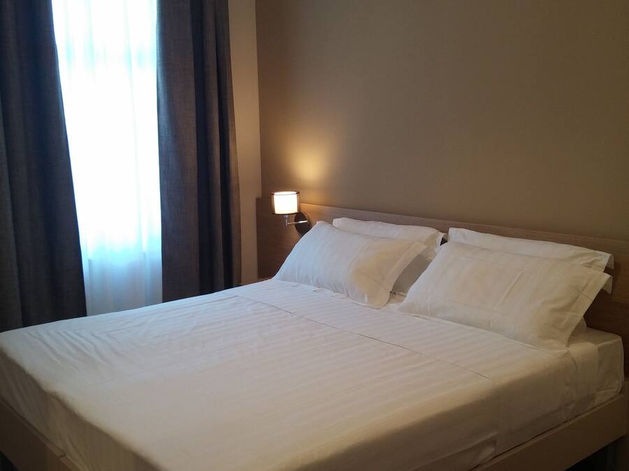 Ein Hotelzimmer mit einem großen Bett, einer Nachttischlampe und einem Fenster mit Vorhängen.