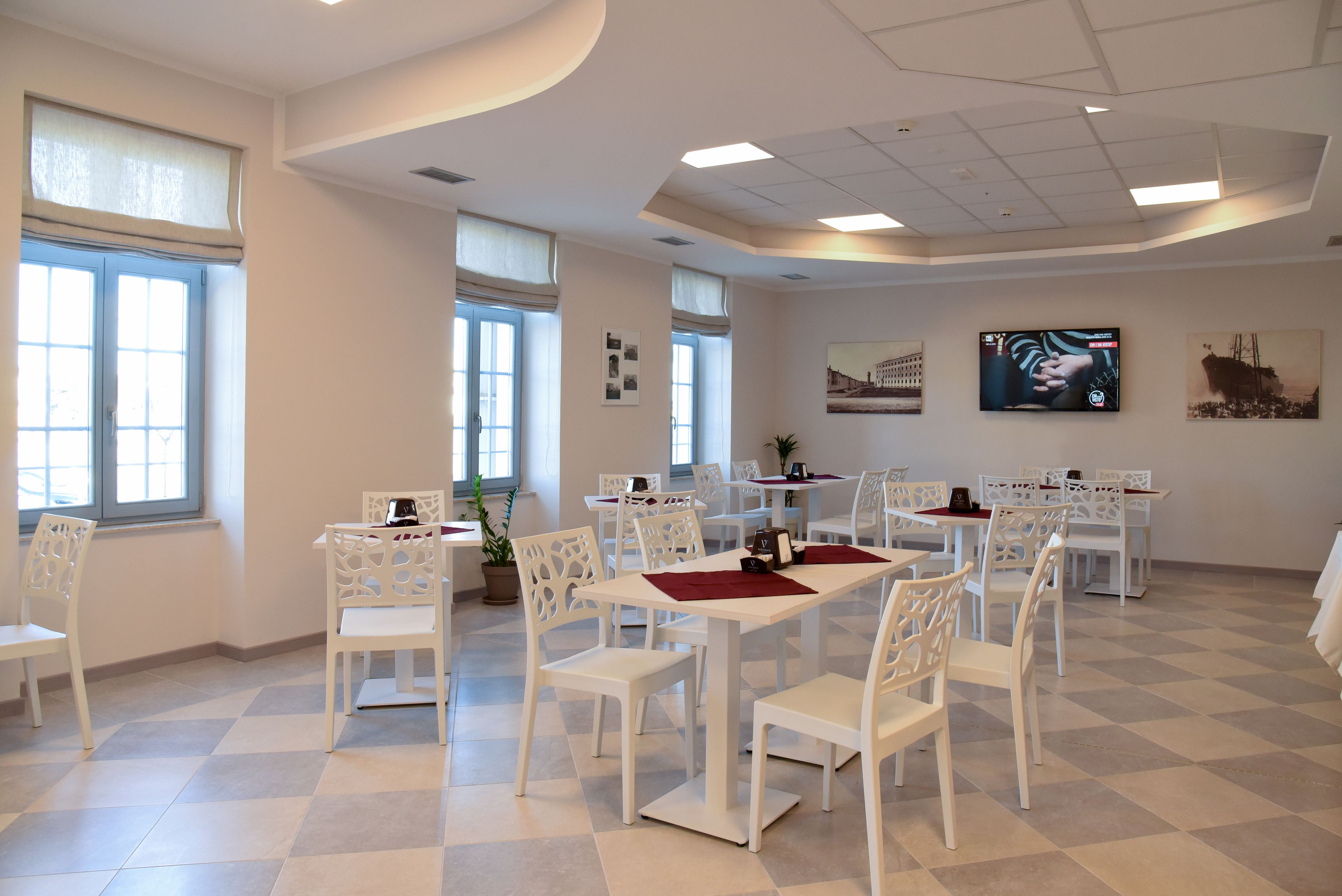 A dining area with white tables and chairs, large windows, and artwork on the walls.
