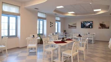 A dining area with white tables and chairs, large windows, and artwork on the walls.