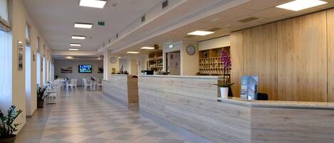 A hotel reception area with a check-in counter, seating area, and a television screen.