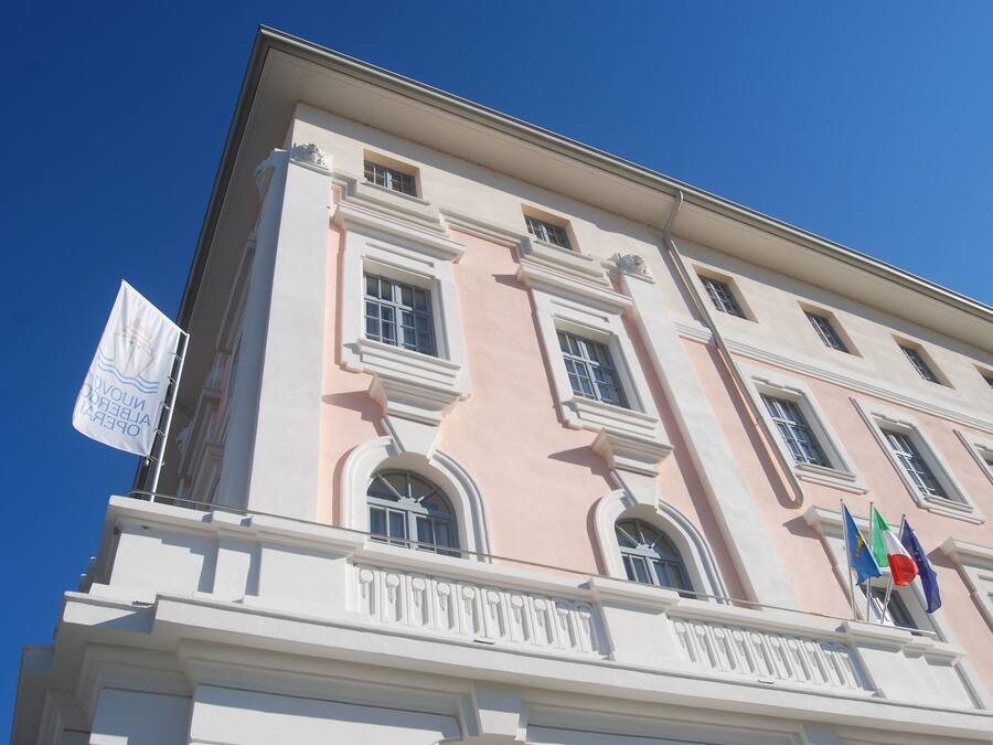 A building with a pink facade, multiple windows, and flags including the Italian flag.