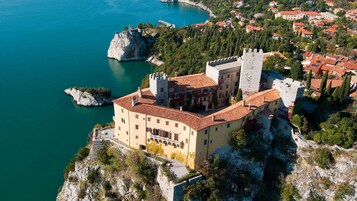 Un castillo con techo de tejas rojas, ubicado en un acantilado con vistas al mar turquesa.