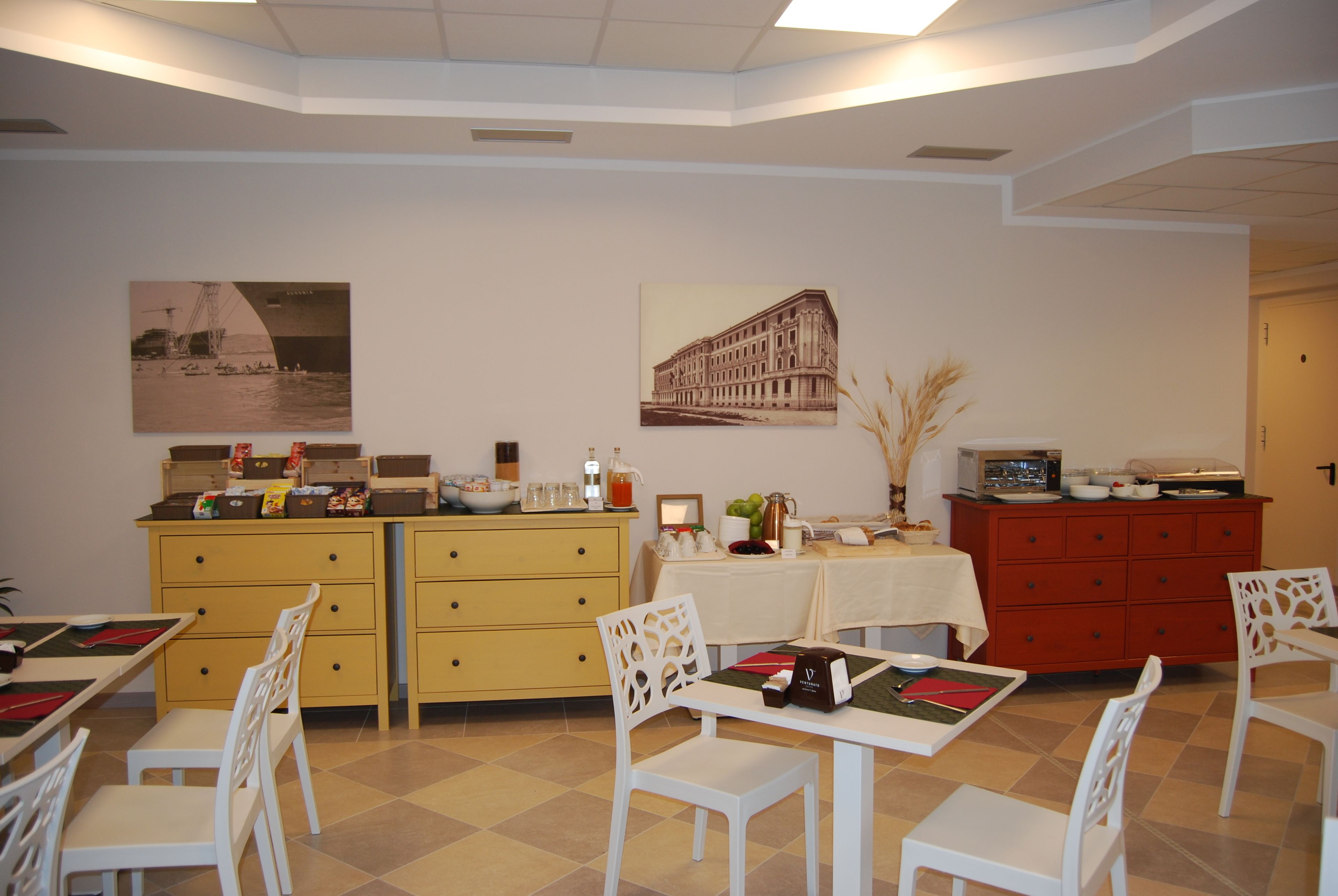 A dining area with a table set for two, a yellow cabinet with drawers, and a red cabinet with a television.