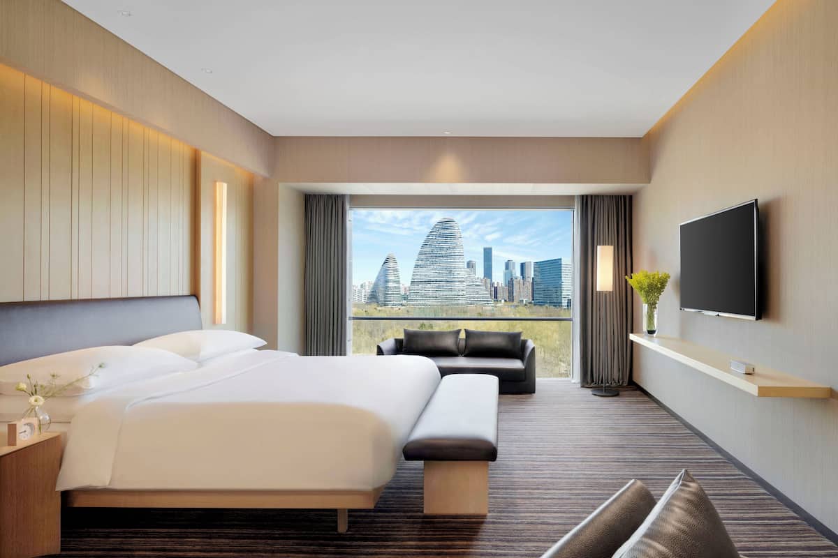 Una habitación de hotel moderna con una cama grande, un sofá, un televisor y vistas a la ciudad.