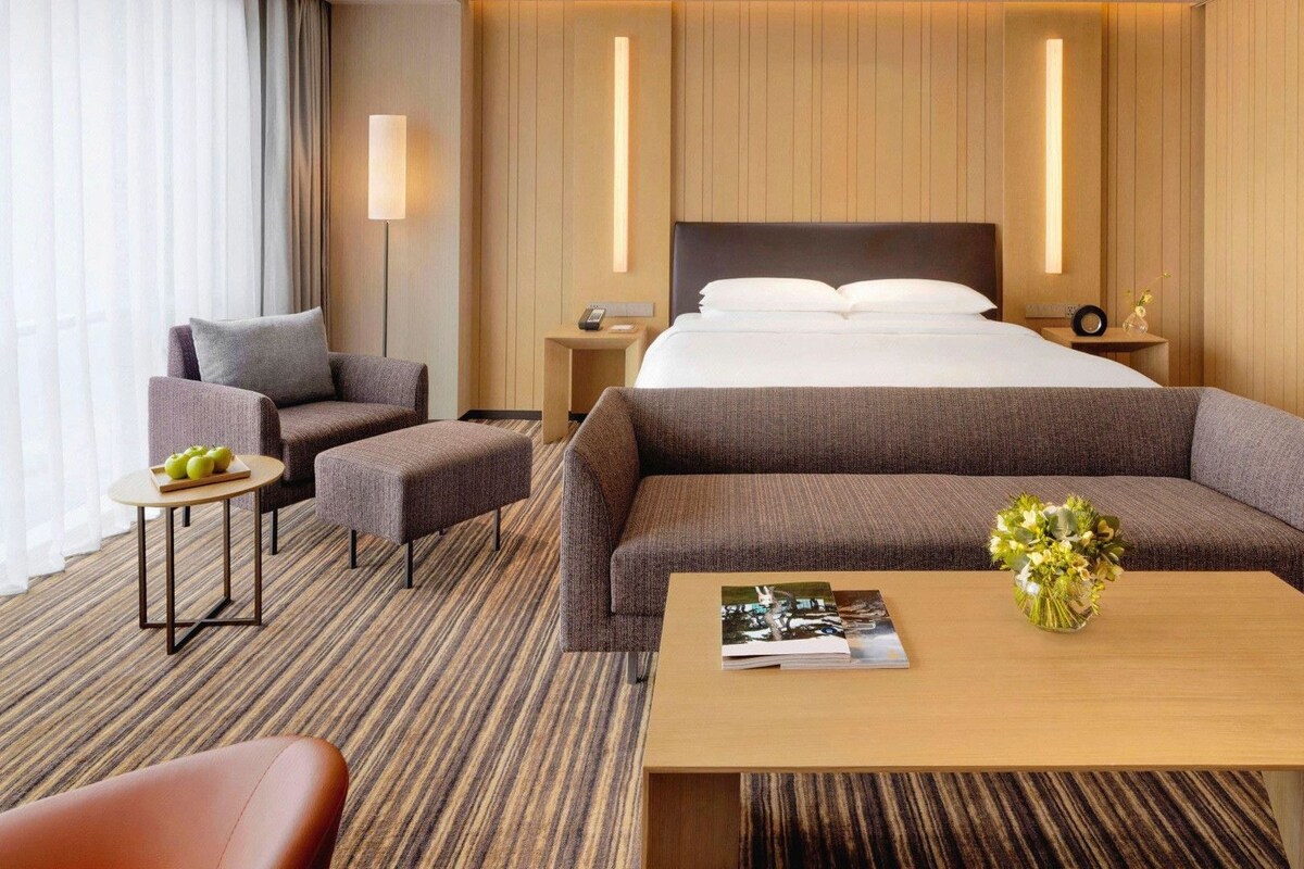 A hotel room with a bed, two sofas, a small table with a vase, and a nightstand with a lamp.