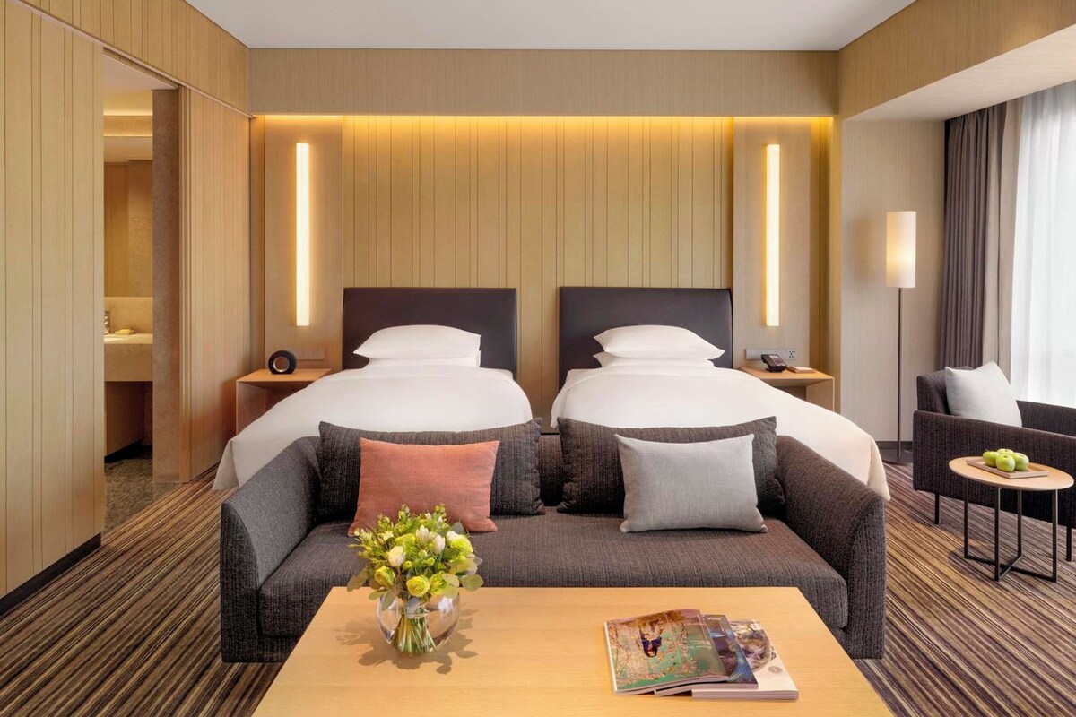 Habitación de hotel con dos camas, un sofá, una mesa de centro y una lámpara.