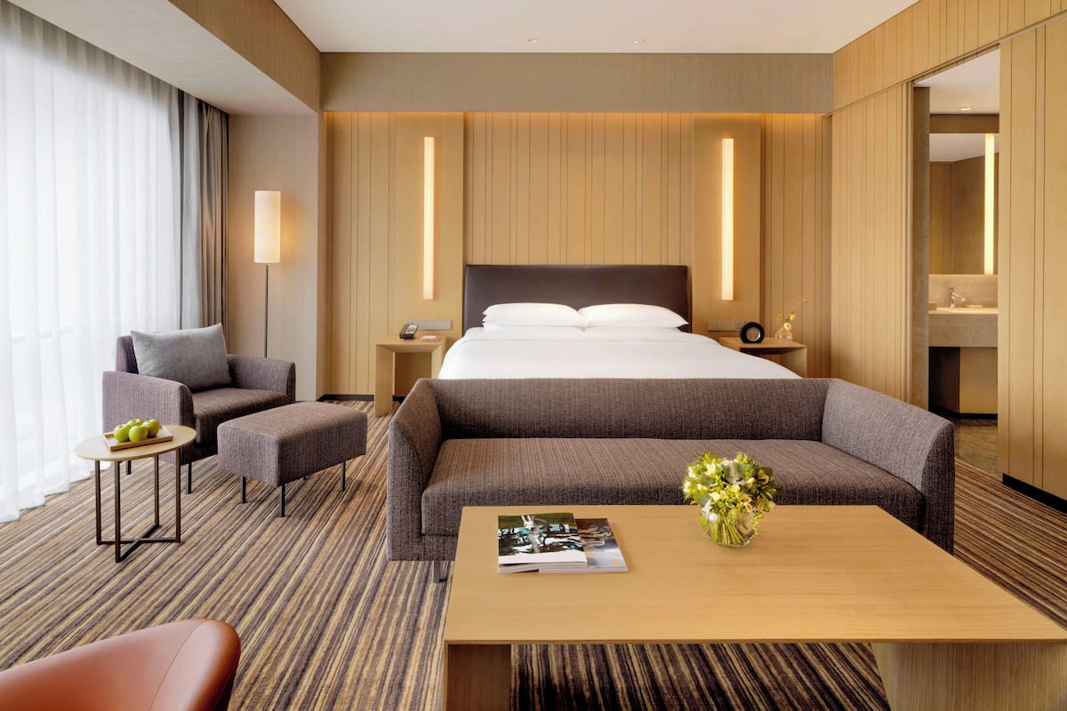 Una habitación de hotel moderna con una cama grande, dos sillones, una mesita y una mesita de noche con lámpara.