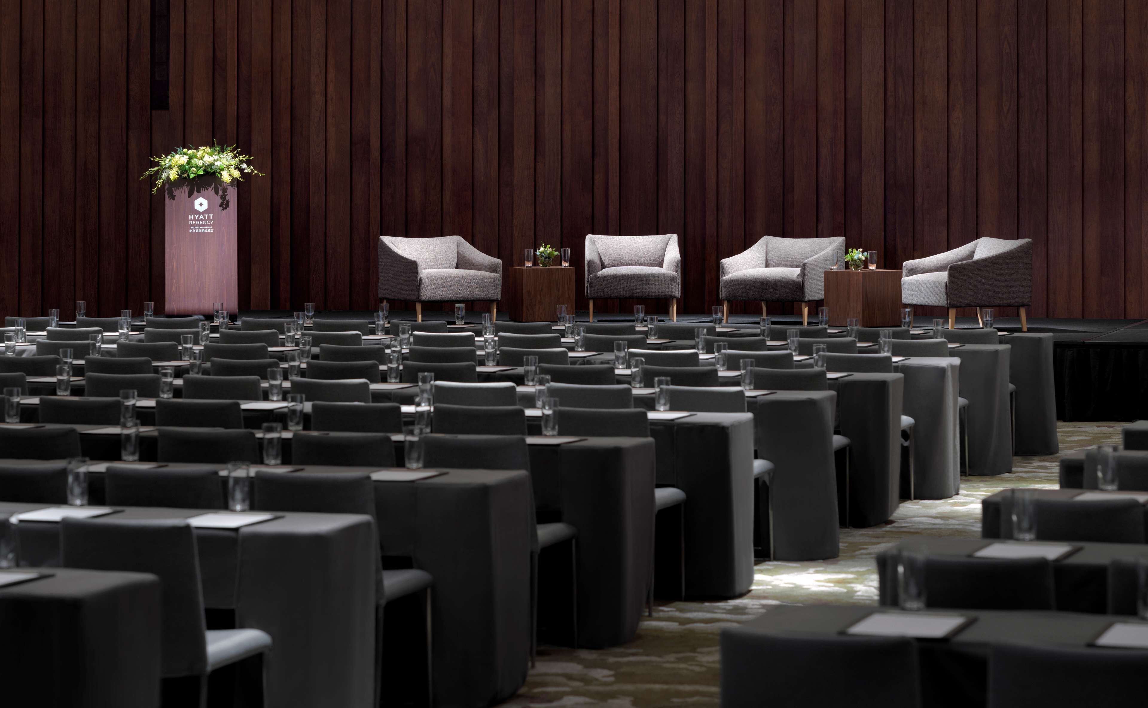 Un salón de conferencias con filas de mesas y sillas, un atril y una planta en maceta.