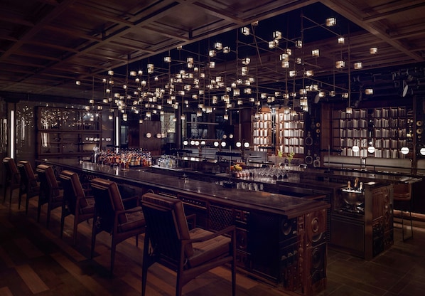 A bar area with wooden chairs, a long bar counter, and hanging lights.