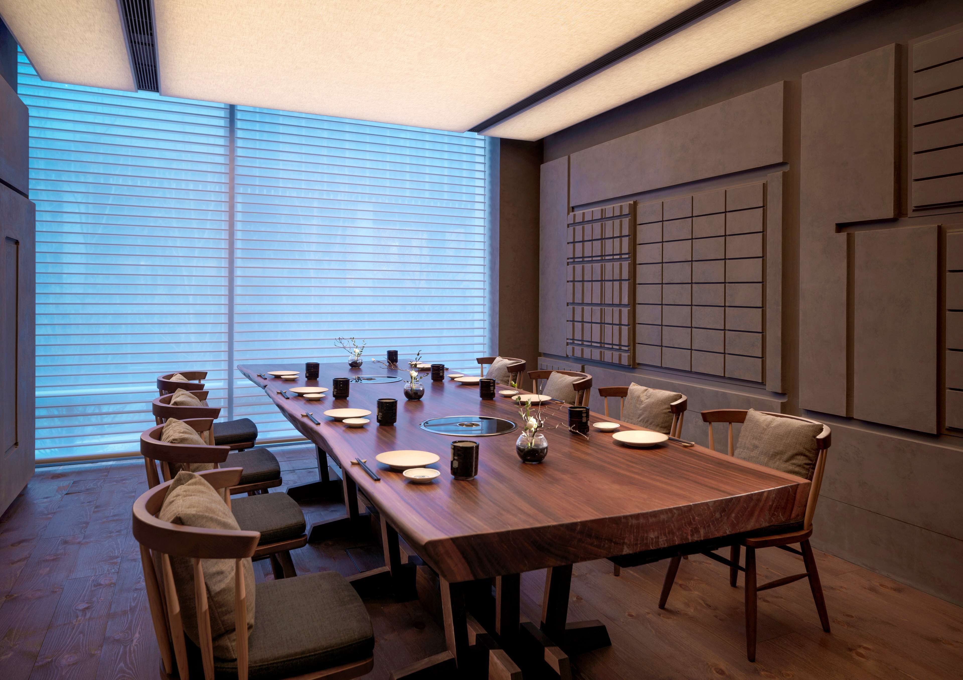 A modern dining area with a long wooden table, multiple chairs, and a decorative vase.