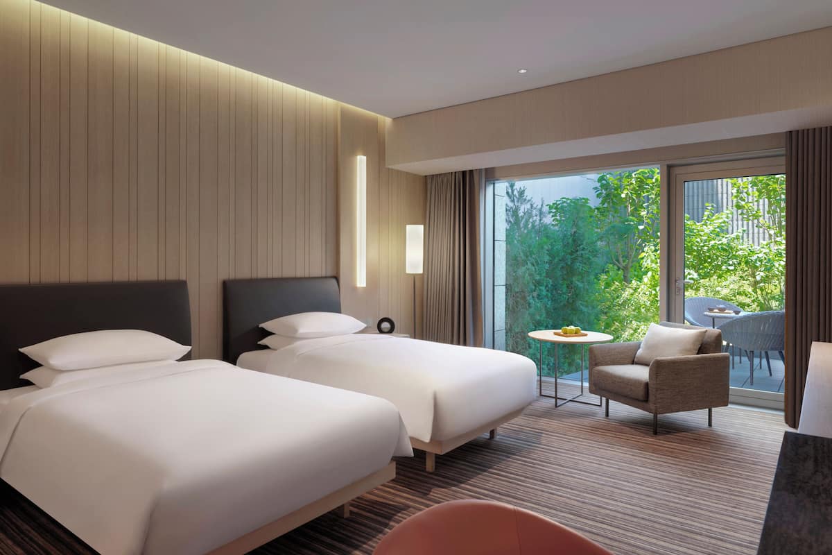 Habitación de hotel con dos camas, una mesita redonda pequeña, una silla y vistas a zonas verdes.