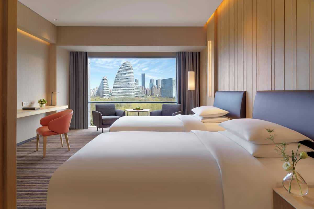Habitación de hotel con dos camas, un escritorio, una silla y vistas a la ciudad.