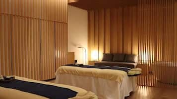 Two beds, a bedside table, and a small table with a lamp, set against a wooden slat wall.
