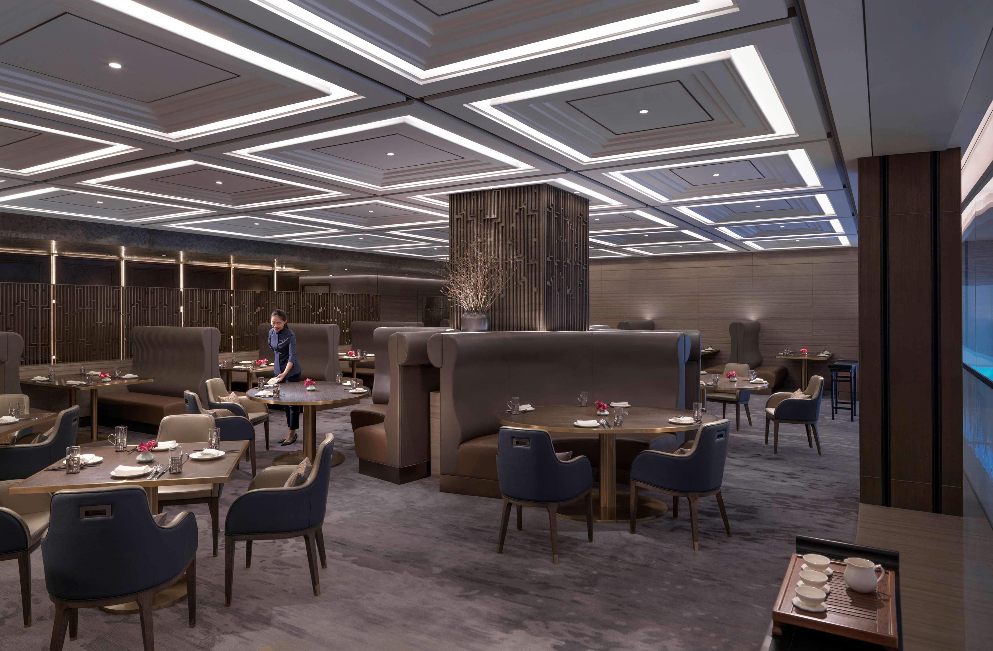 A modern restaurant with high ceilings, geometric lighting, and plush seating.