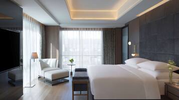 Une chambre d’hôtel moderne dotée d’un grand lit, d’un téléviseur à écran plat, d’un canapé et d’une petite table avec une lampe.